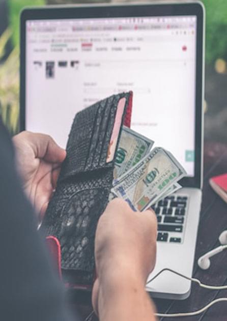 person holding hundred dollar bills in front of laptop